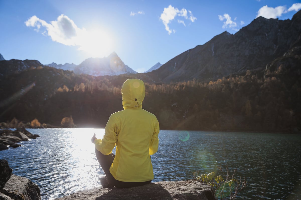 Mujer meditando junto a un lago de alta montaña