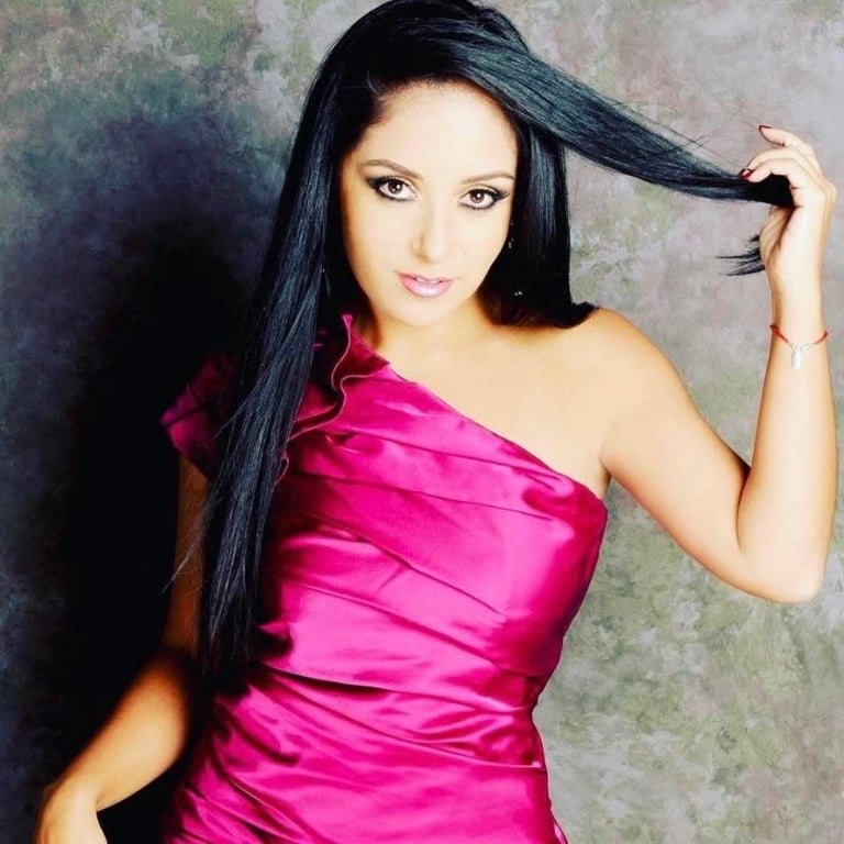 Woman with long black hair wearing a bright pink strapless dress, posing against a textured neutral background