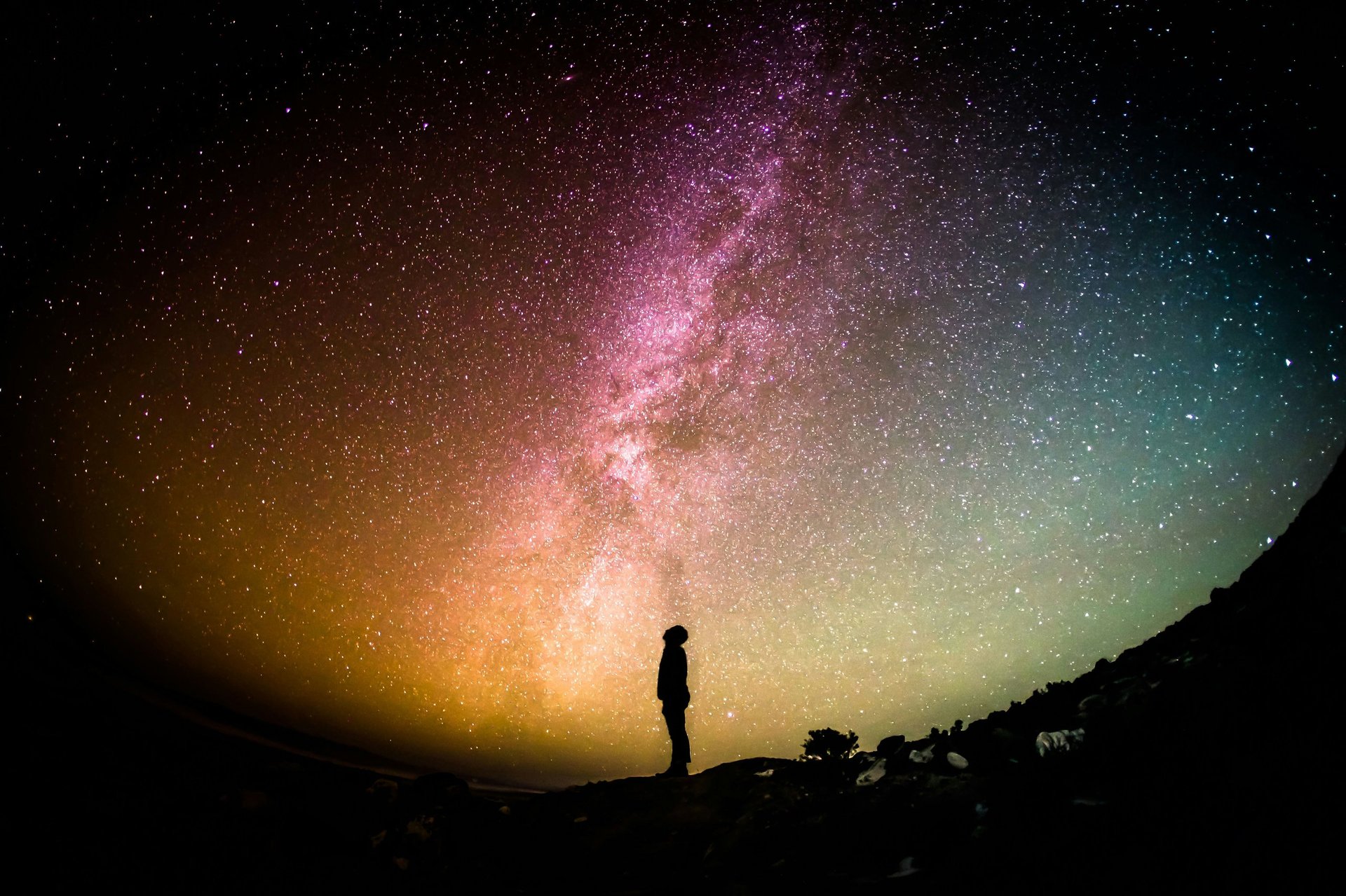 Silhouette of a person standing under the Milky Way galaxy at night with colorful stars and nebula overhead